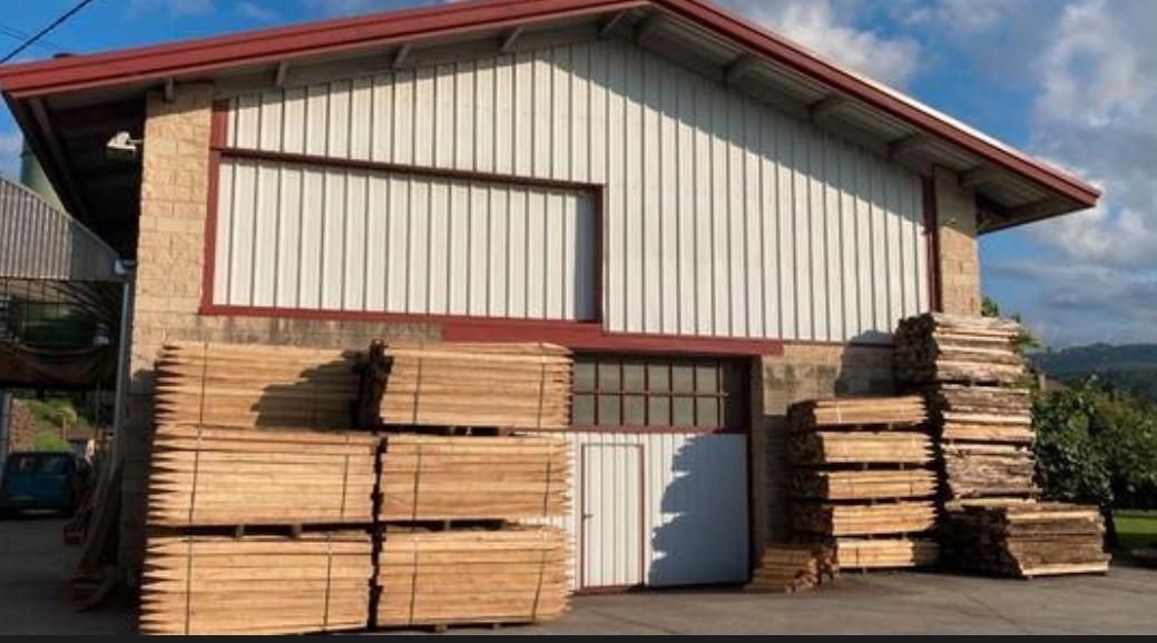 Pilas de postes de madera puntiagudos sobre tierra y vigas de madera, al aire libre.