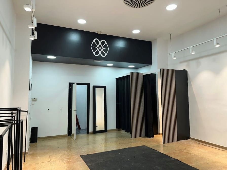 Interior de tienda de ropa vacía con probadores, espejos y logotipo sobre la entrada.