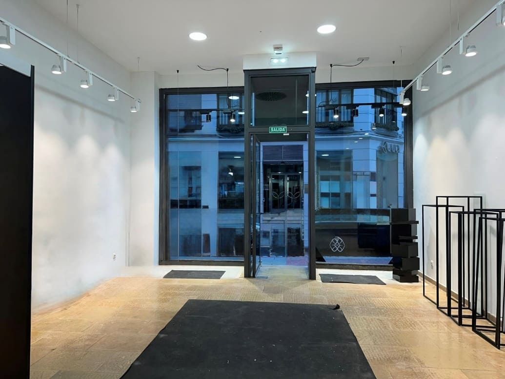 Local comercial vacío con gran escaparate de vidrio, pisos de madera, paredes blancas e iluminación de riel.