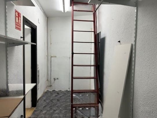 Habitación interior con una escalera alta, una puerta oscura y un extintor en la pared.