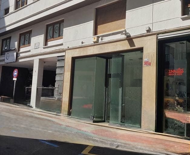 Edificio con escaparates de cristal, persianas cerradas y vista a la calle.