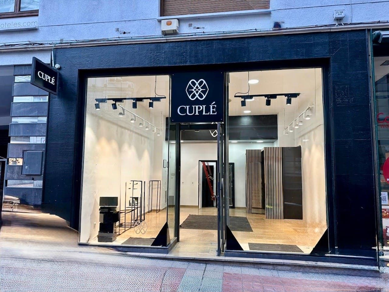 Exterior de una tienda CUPLÉ. Fachada oscura, grandes ventanales y puerta abierta. En el interior, se ven percheros.