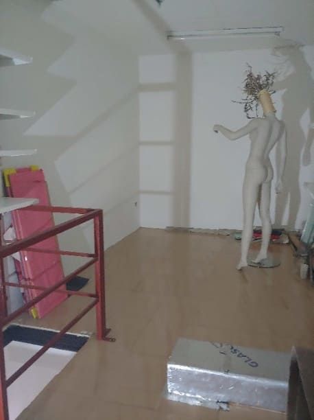 Interior de tienda vacío con maniquí, piso de madera, barandilla de metal rojo y paredes blancas.