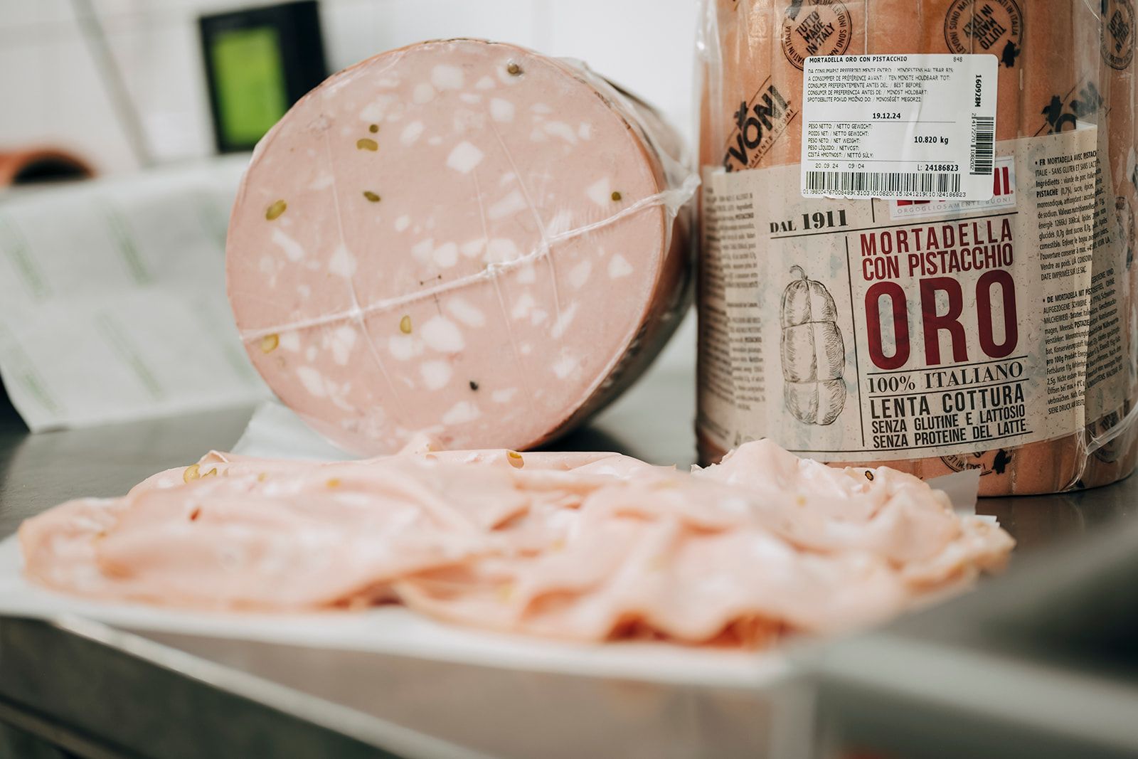 Zwei Scheiben Mortadella liegen auf einer Theke neben einem Behälter mit Aufschnitt.