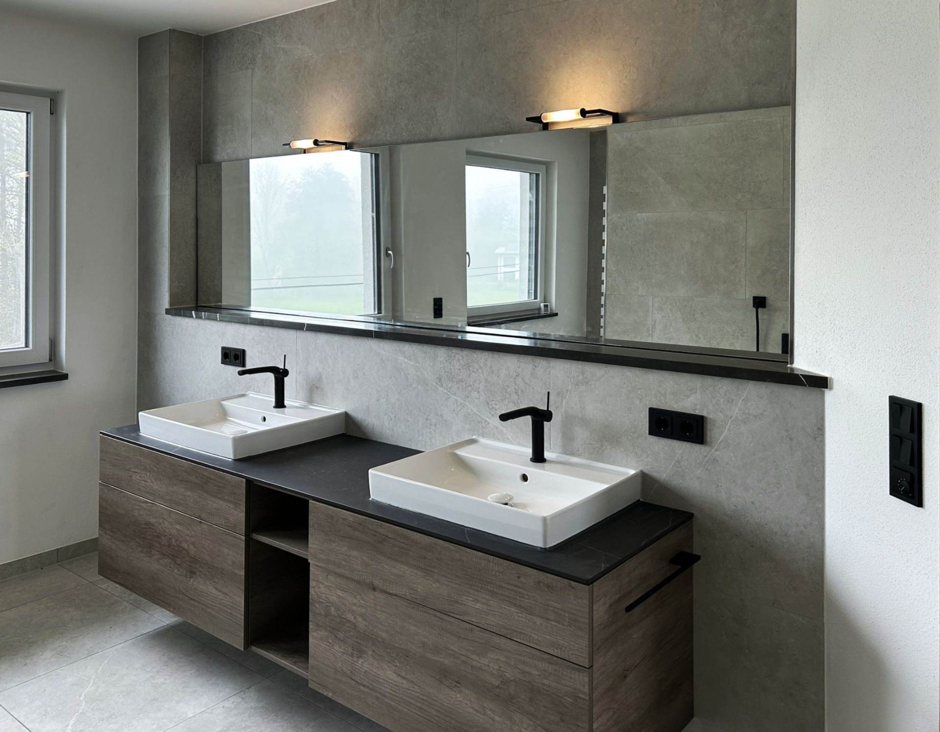 Modernes Badezimmer mit zwei Waschbecken, Spiegeln und Wandleuchten; neutrale Farbtöne.