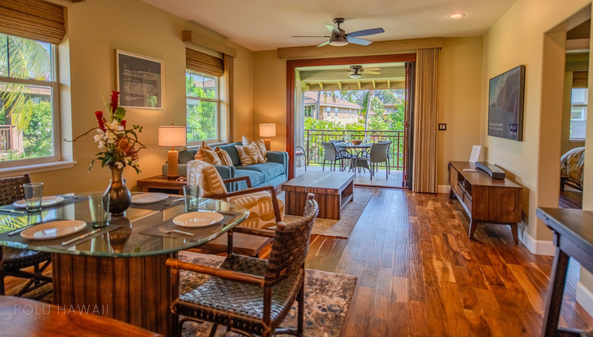A living room with hardwood floors , a couch , a table , chairs and a television.