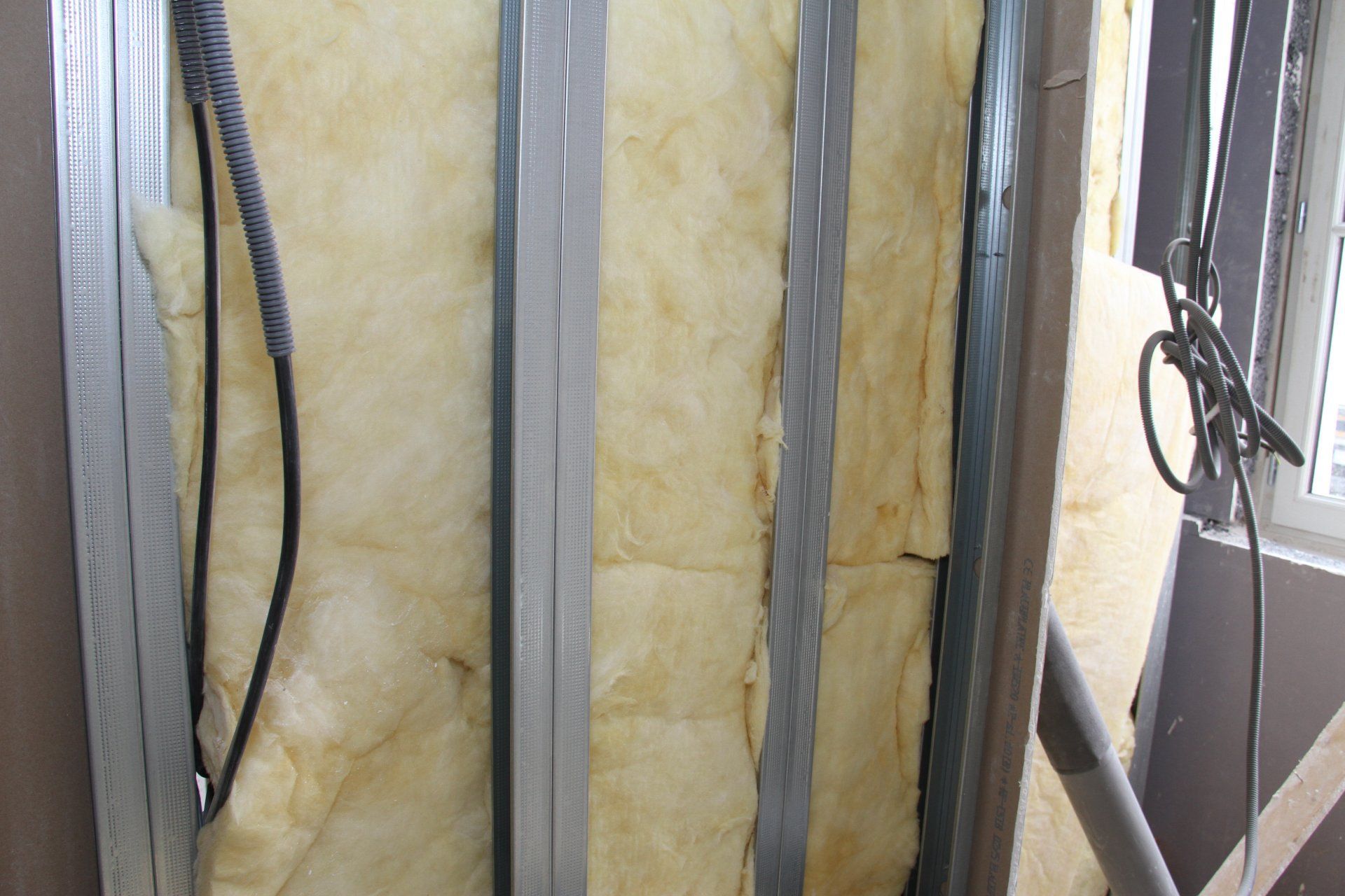 Montants muraux isolés avec des rouleaux de laine de verre jaune et une ossature grise à l'intérieur d'une pièce non finie