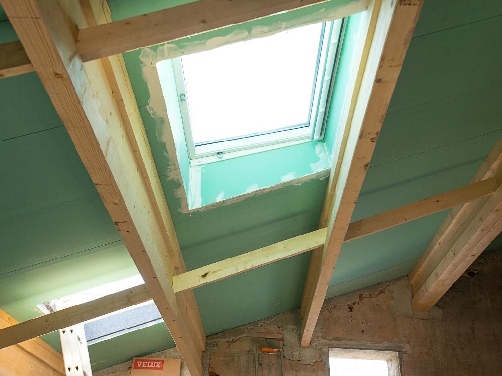 Plafond intérieur avec poutres en bois apparentes et puits de lumière laissant entrer la lumière du jour.