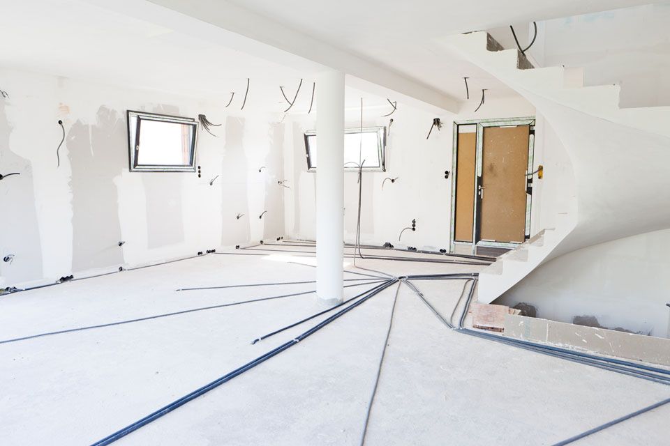 Pièce blanche vide en cours de rénovation, avec des fils électriques apparents, une colonne et une porte en bois au fond.
