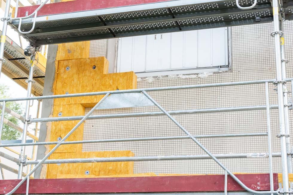 Échafaudages devant un bâtiment en briques avec une porte en contreplaqué jaune et des panneaux de fenêtres blancs