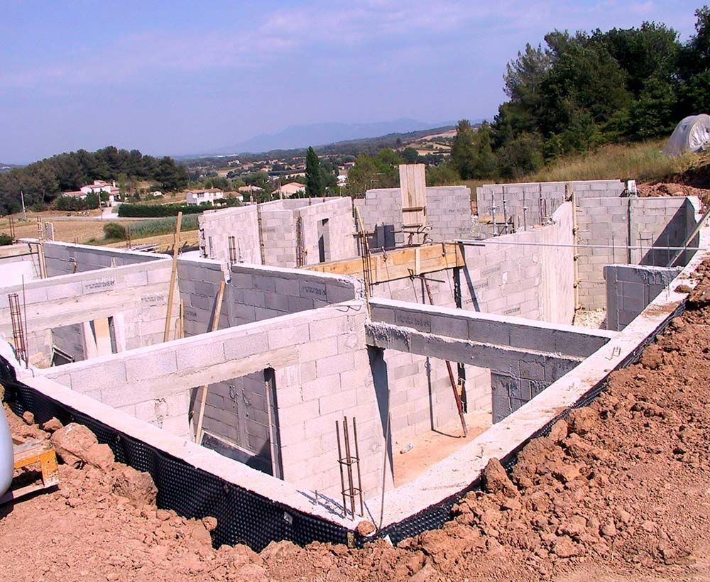 Fondation en blocs de béton en construction à flanc de colline, avec des barres d'armature apparentes et de la terre autour.