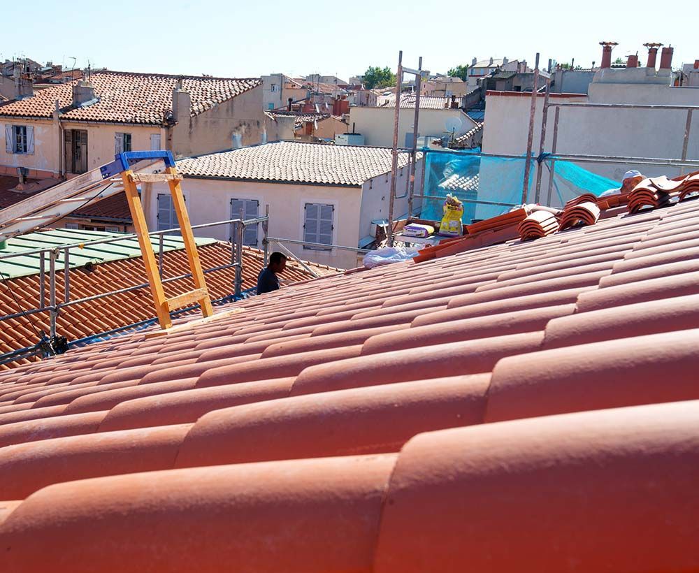Vue depuis un toit avec des tuiles rouges, une échelle et des bâtiments de la ville sous un ciel dégagé.