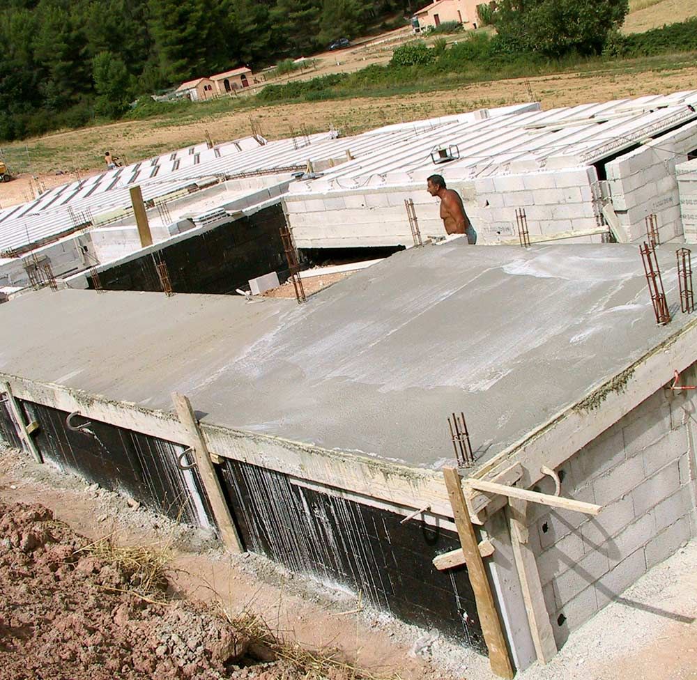 Chantier de construction d'une maison en parpaings, murs partiellement construits et un ouvrier sur le toit