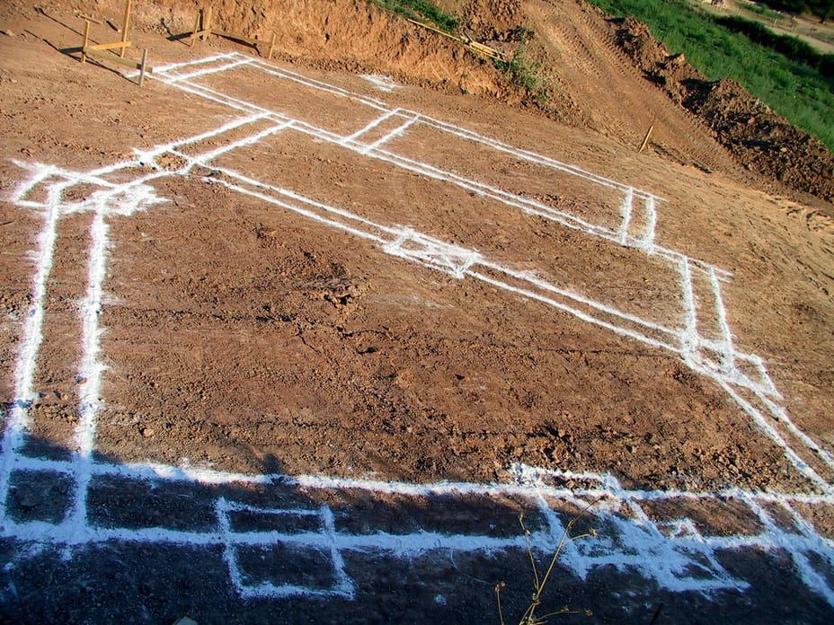 Un contour à la craie blanche délimite les fondations d'une maison sur un terrain en pente.
