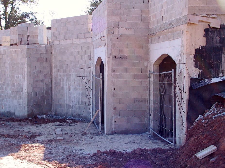 Structure en pierre partiellement construite avec des portes cintrées et des portails métalliques dans un espace extérieur poussiéreux