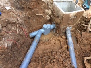 Des tuyaux en PVC bleus ont été installés dans une tranchée excavée près d'une structure en béton.