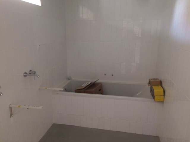 Baignoire blanche vide dans une salle de bains carrelée, avec un seau jaune sur le rebord droit.