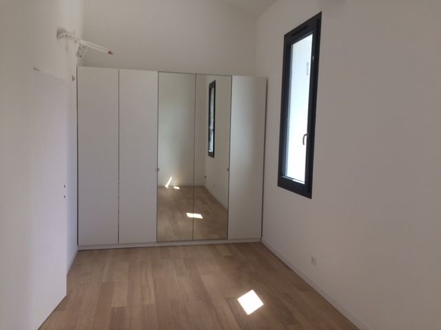 Pièce blanche vide avec parquet, armoire à miroirs et haute fenêtre étroite