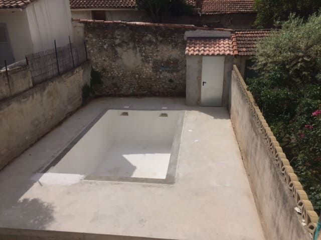Piscine rectangulaire vide dans une cour entourée de murs et de pierres et de carreaux.