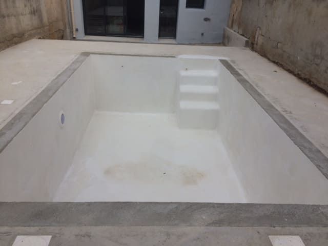 Piscine rectangulaire vide avec intérieur blanc et contour en béton dans un patio