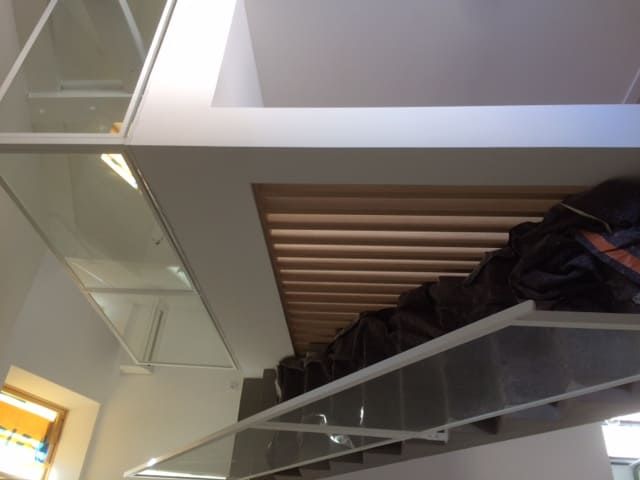 Intérieur de loft avec mezzanine à balustrade en verre, plafond à lattes de bois et un sac sombre sur l'étagère supérieure.