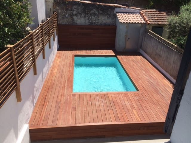 Petite terrasse à l'arrière avec une piscine rectangulaire turquoise et une clôture en bois.