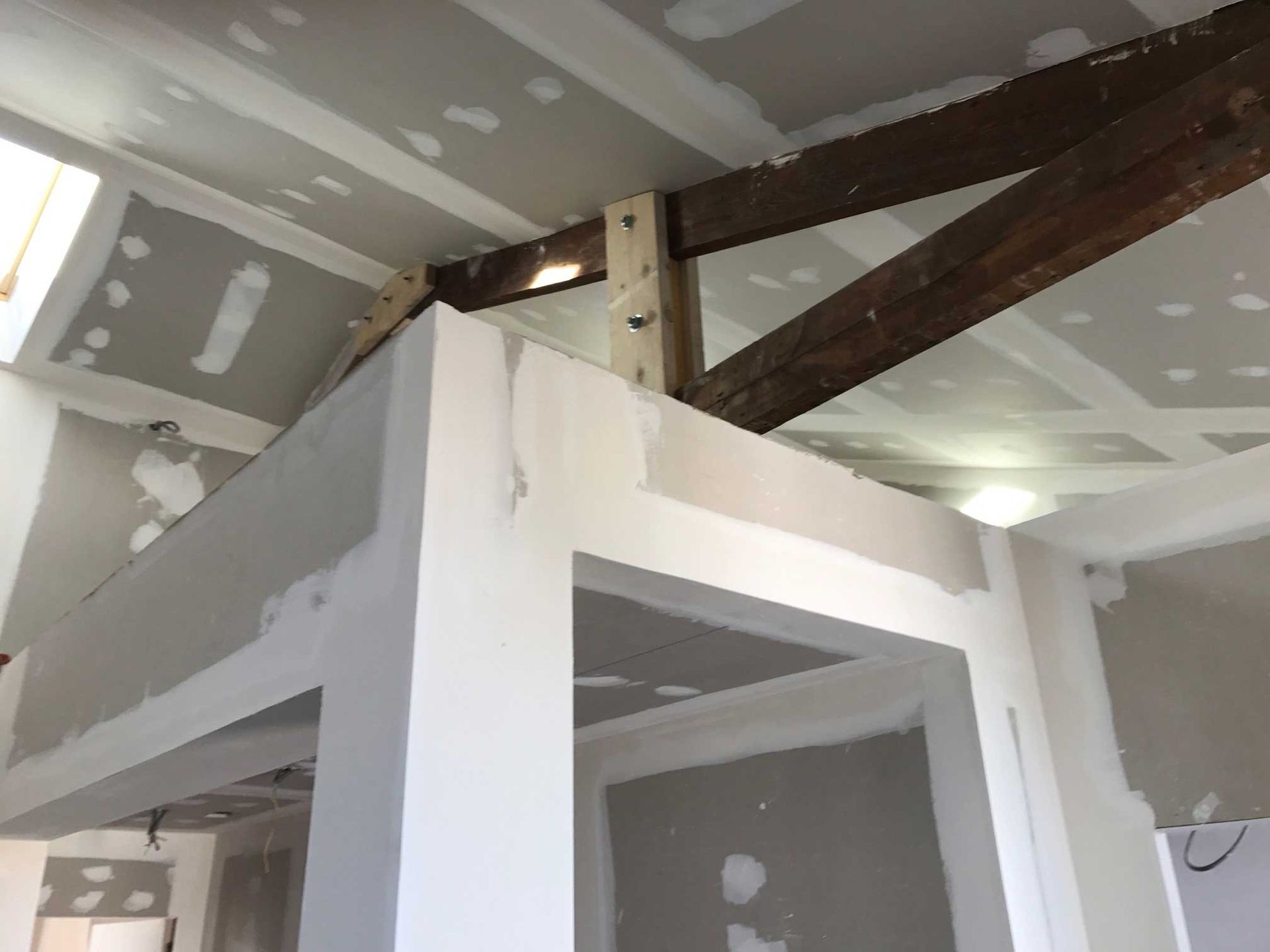 Pièce inachevée avec poutres en bois apparentes et plaques de plâtre jointoyées au plafond et aux murs