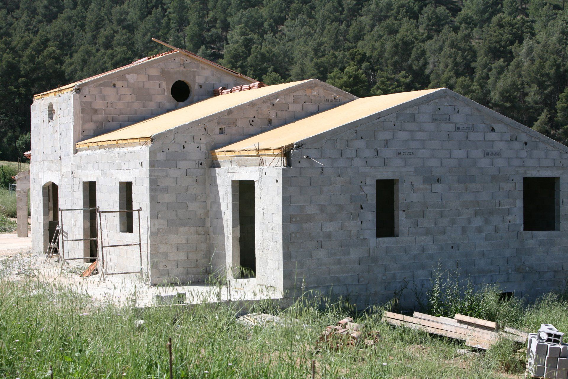 Maison en pierre partiellement construite dans un champ herbeux avec une colline boisée à l'arrière.