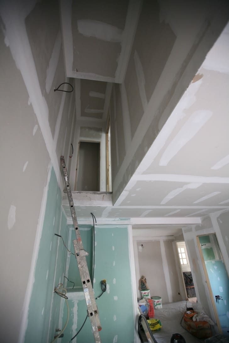 Intérieur en travaux avec cloisons sèches, échelle et plafond non fini dans un couloir étroit