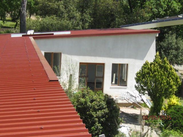 Maison blanche au toit rouge, entourée d'arbres et d'arbustes verts.