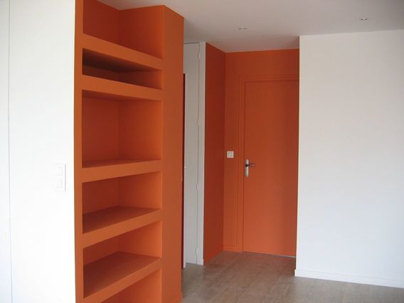 Pièce vide avec des étagères encastrées orange et un mur blanc près d'une porte