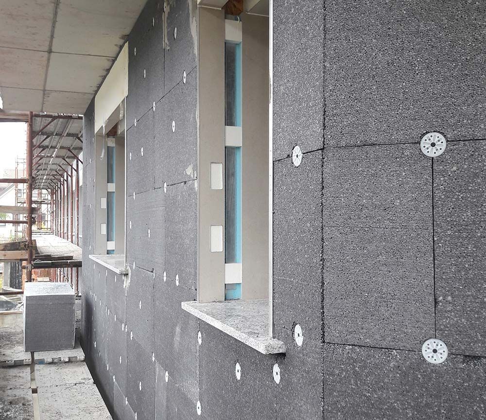 Extérieur du bâtiment partiellement fini avec panneaux d'isolation gris et ouvertures de fenêtres en construction