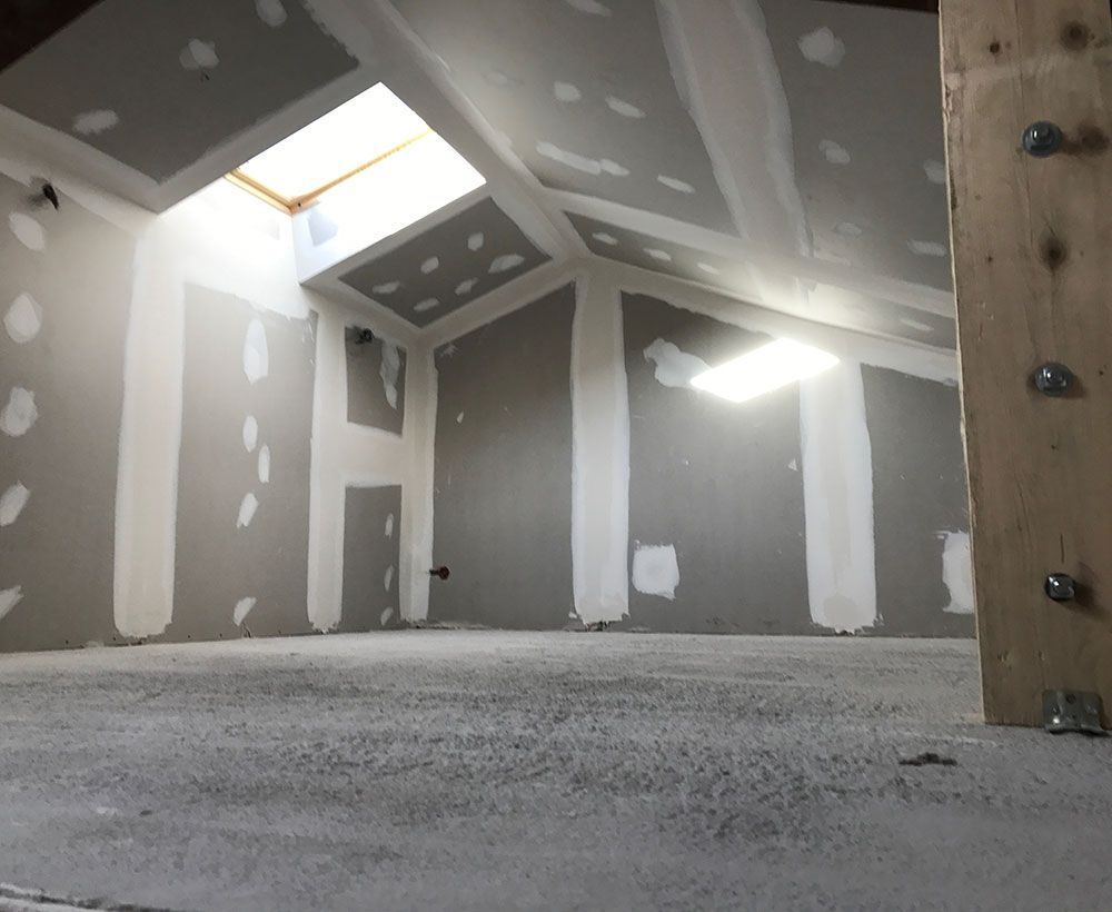 Grenier non aménagé avec cloisons sèches, puits de lumière et poutre en bois apparente.