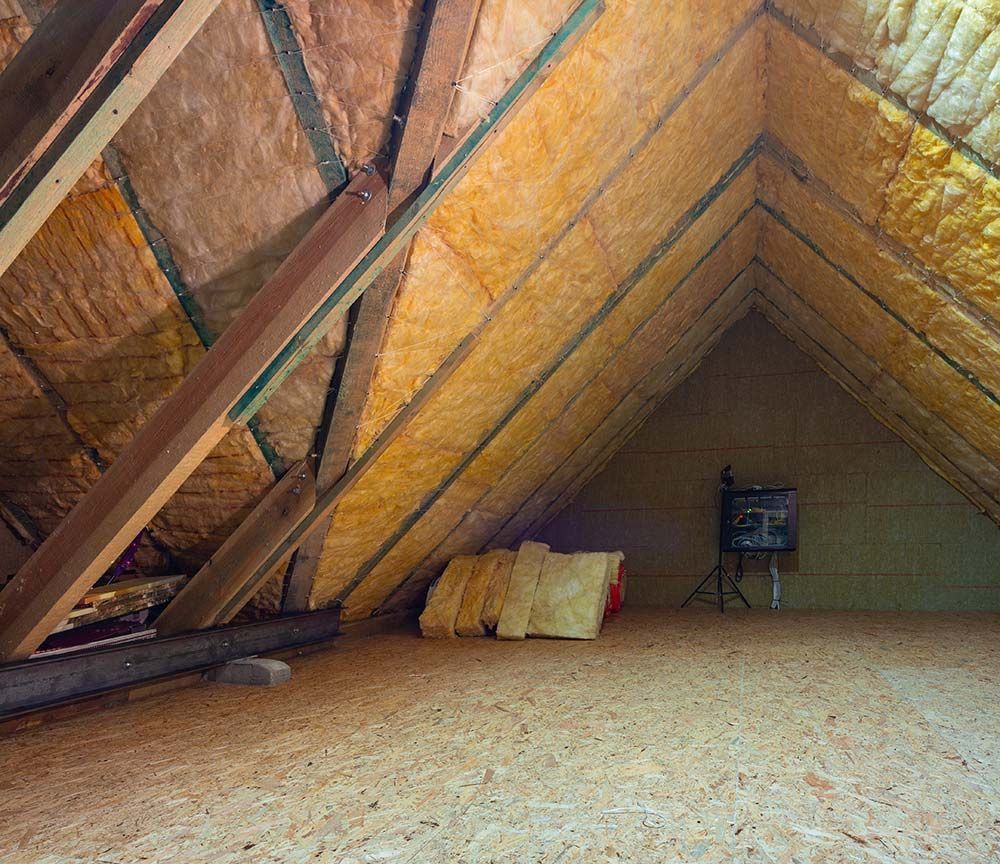 Grenier avec isolation apparente, poutres en bois inclinées et une petite chaise dans un coin