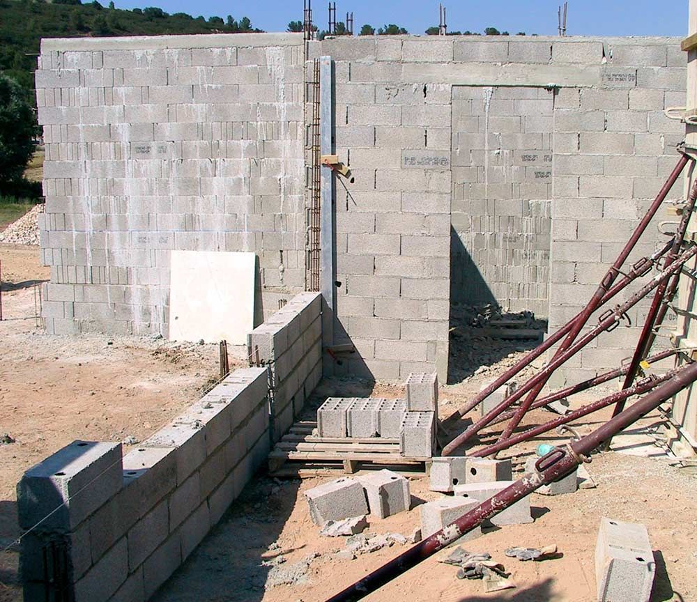 Structure en parpaings partiellement construite avec échafaudages et matériaux de construction sur un terrain en terre battue