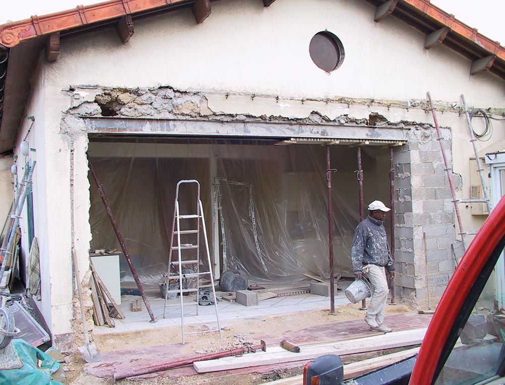 Maison en rénovation avec garage ouvert, échelle et ouvrier en train d'enlever les débris