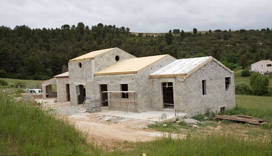Maison en pierre en construction dans une zone rurale herbeuse avec des arbres en arrière-plan