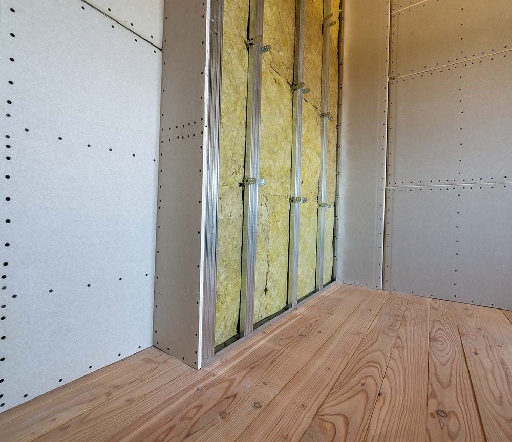 Intérieur d'une pièce inachevée avec sol en contreplaqué, murs en plaques de plâtre et isolation jaune apparente dans une section de mur