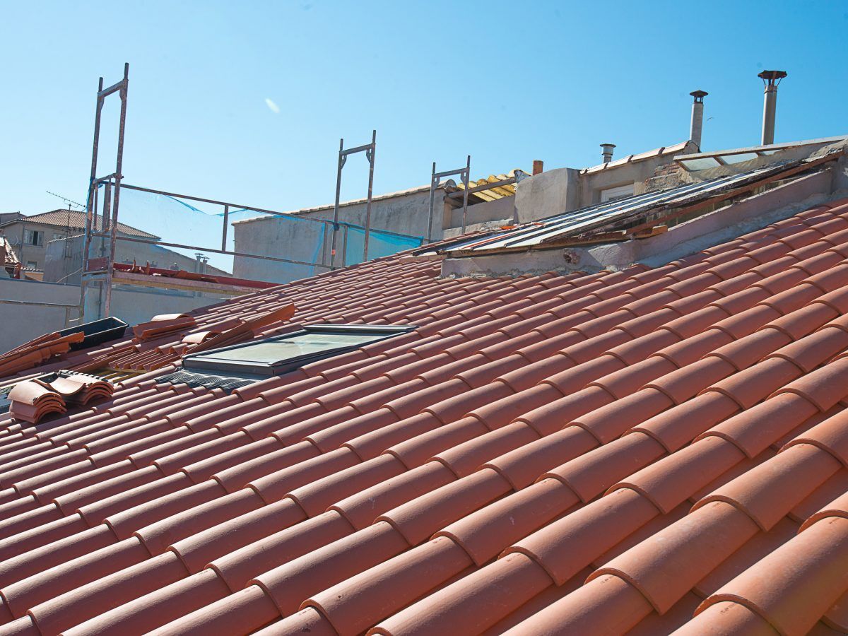 Toits de tuiles rouges en construction, avec des échafaudages et un ciel bleu clair.