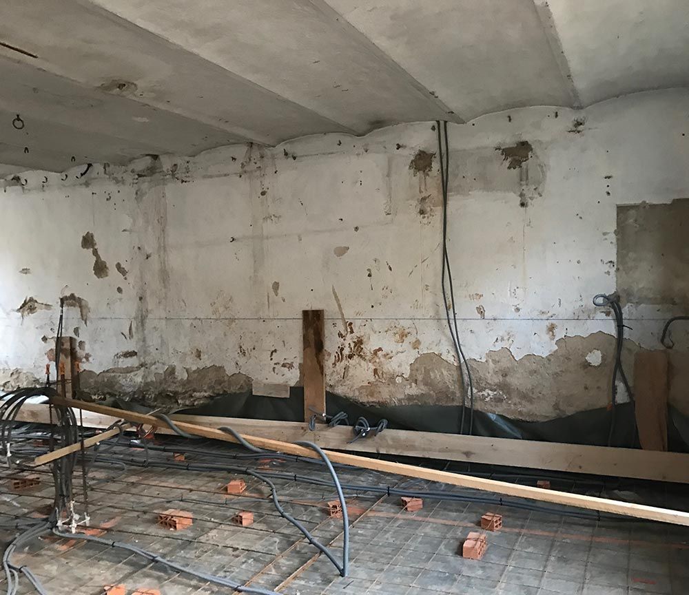 Pièce en béton endommagée, murs qui s'écaillent, câbles électriques apparents et débris de construction éparpillés.