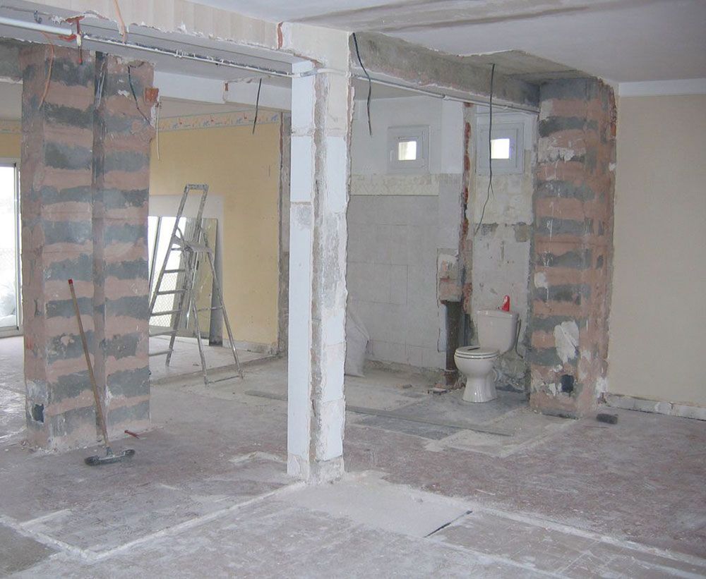 Intérieur inachevé avec colonnes de briques apparentes, échelle dans l'arrière-salle et toilettes en construction.