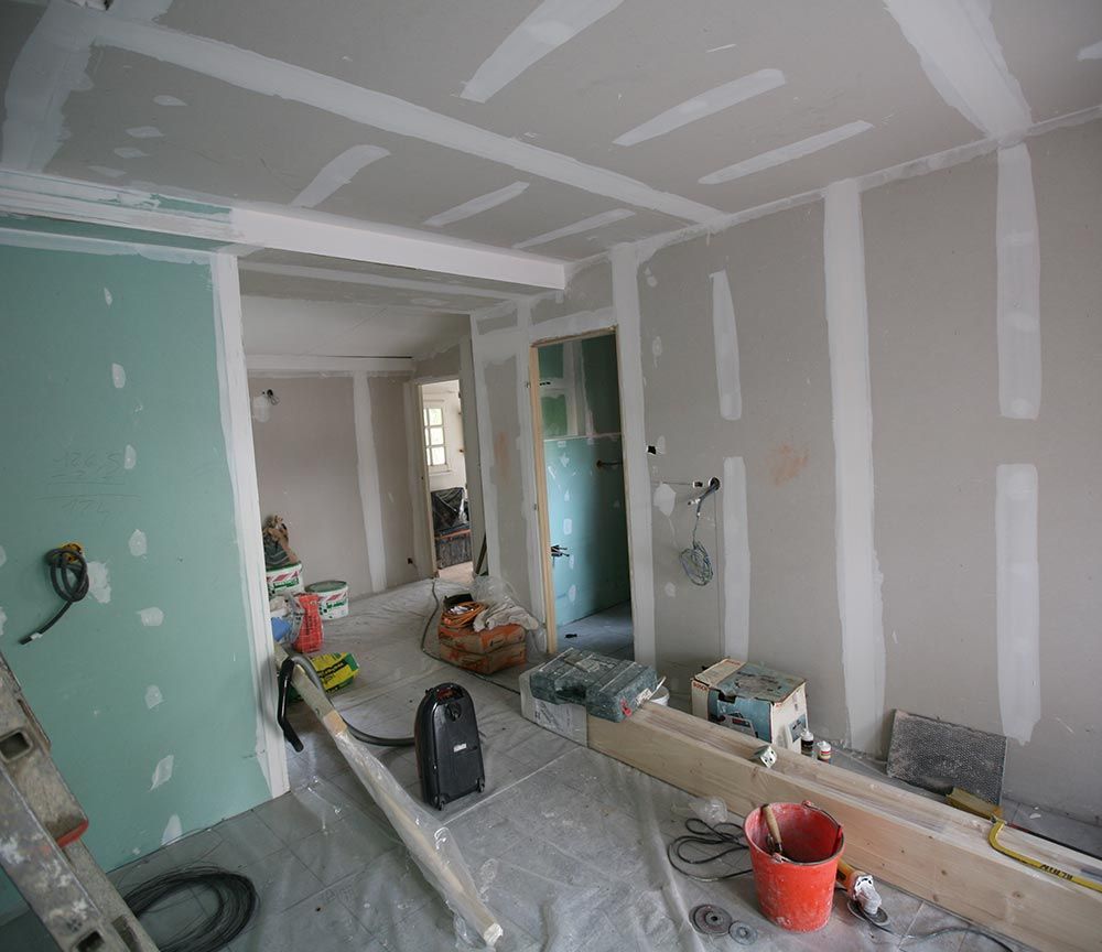 Cuisine en cours de rénovation, inachevée, avec des plaques de plâtre, des outils et des matériaux de construction éparpillés sur le sol.