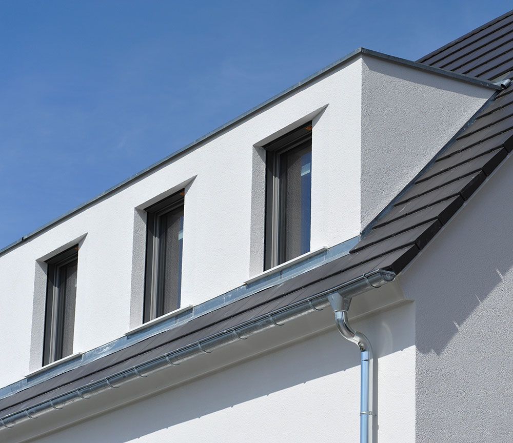 Lucarne d'une maison blanche à trois fenêtres et toit gris foncé sur fond de ciel bleu