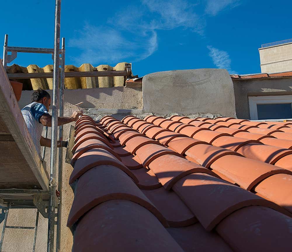 Ouvrier sur un échafaudage installant des tuiles en terre cuite sur un toit ensoleillé sous un ciel bleu