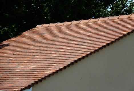Toit de tuiles rouges sur une maison se détachant sur des arbres vert foncé