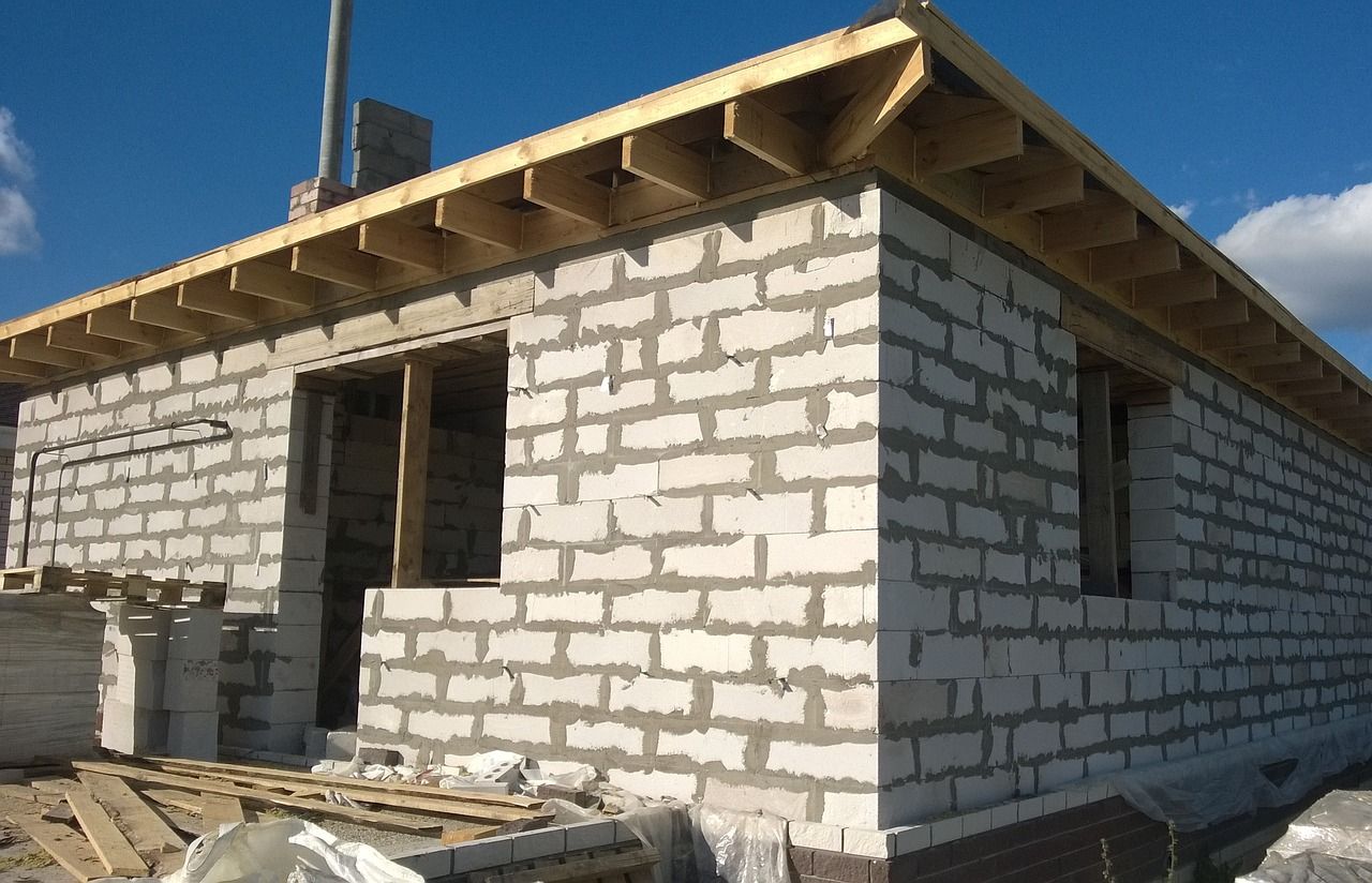 Maison en briques blanches inachevée, en construction, avec une charpente de toit en bois apparente et un ciel bleu.