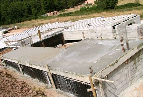 Fondations de maison en béton partiellement construites avec dalles de toiture dans une zone rurale boisée