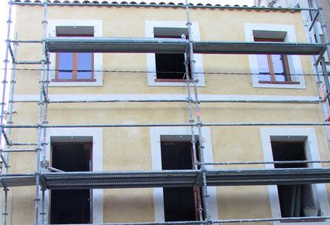 Échafaudages sur la façade d'un bâtiment en stuc jaune avec plusieurs fenêtres ouvertes.