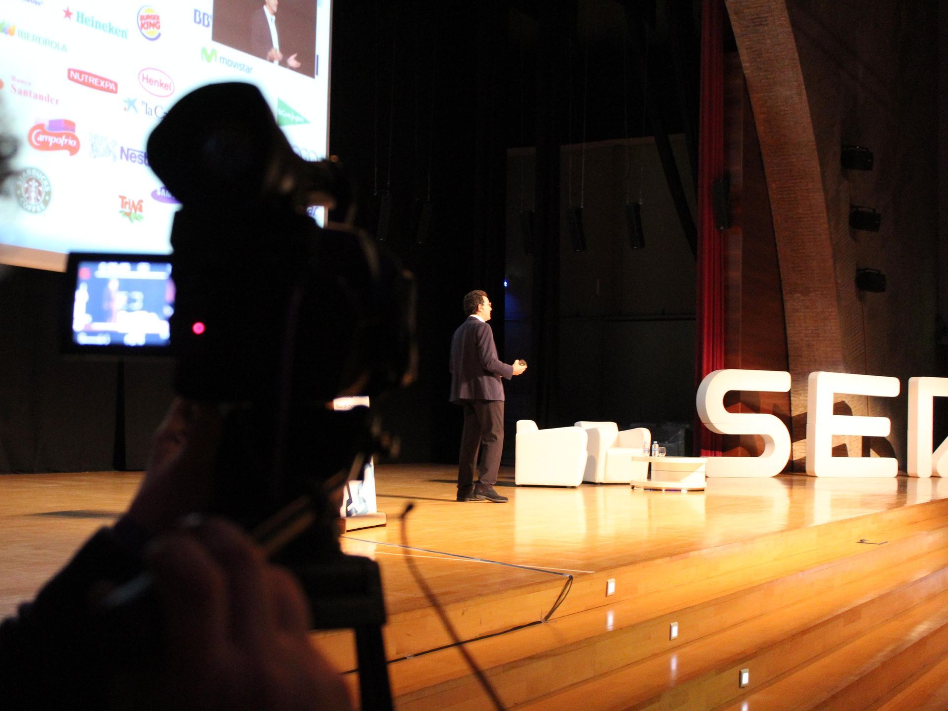 Un hombre está dando una presentación en un escenario frente a un cartel que dice sed