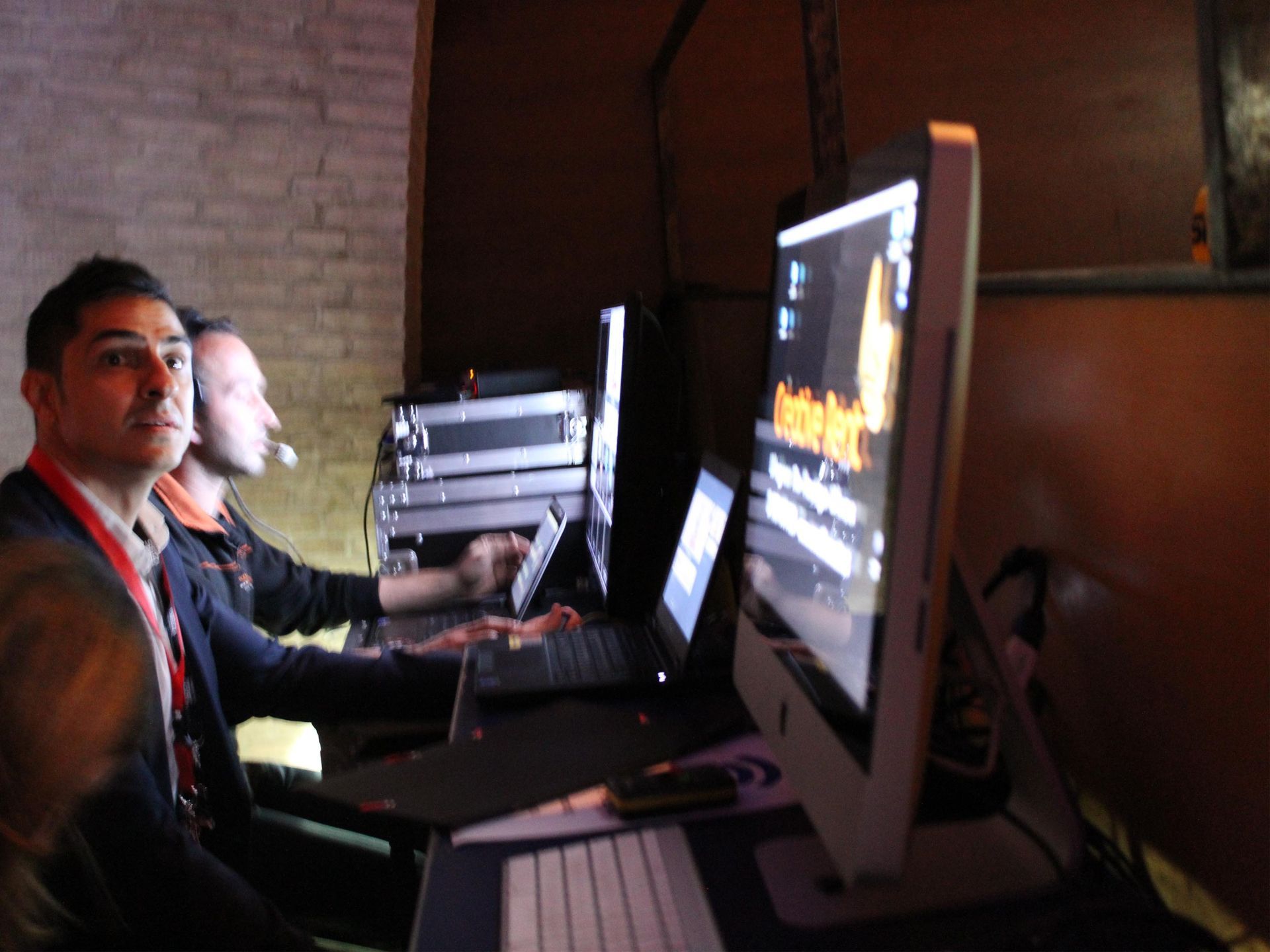 Dos hombres están sentados frente a monitores de computadora y una computadora portátil.